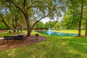 Escape to a serene park setting with a tranquil pond, lush greenery, and a clear sky. Enjoy a peaceful spot on the bench.