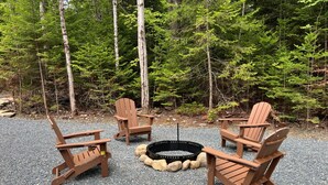 A fire pit surrounded by wooden Adirondack chairs in a gravel area with trees in the background. - New Construction Barn style- Minutes from Skiing and Lakes (Wilmington)