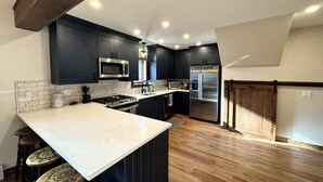 A modern kitchen with dark cabinetry, a large island, and stainless steel appliances. - New Construction Barn style- Minutes from Skiing and Lakes (Wilmington)