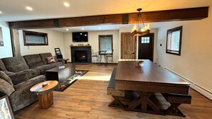A spacious living room with a wooden dining table, a sofa, and a fireplace. - New Construction Barn style- Minutes from Skiing and Lakes (Wilmington)
