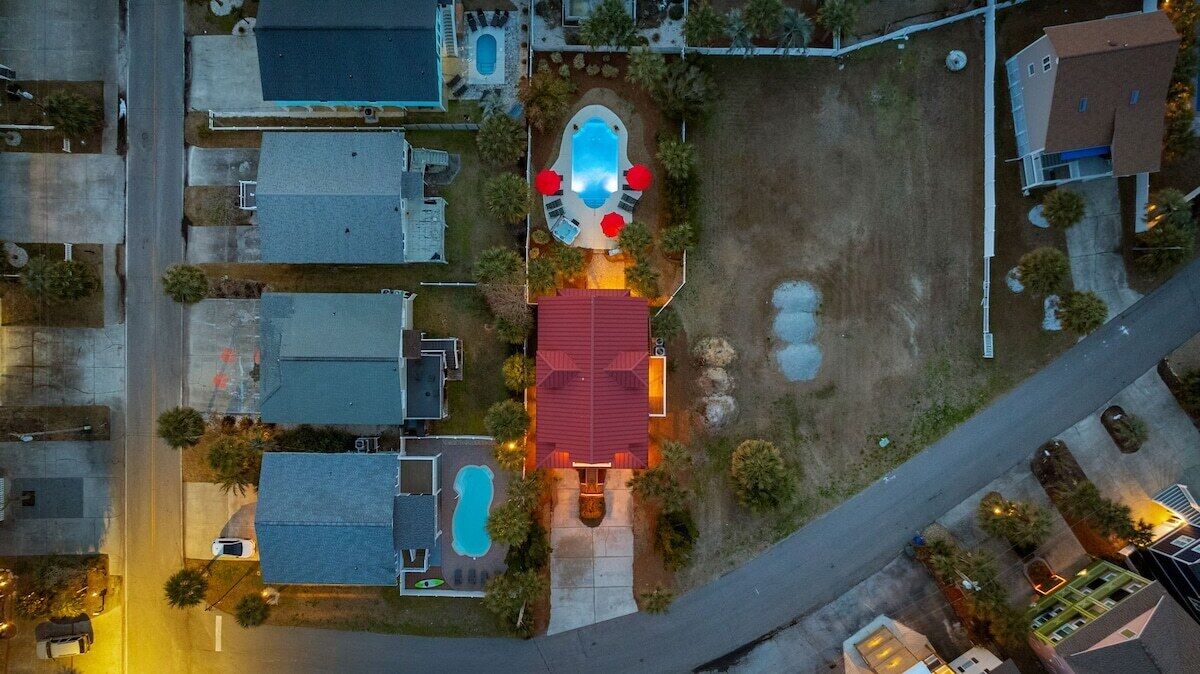 An aerial view of a residential area with a swimming pool, a red-roofed house, and adjacent buildings.