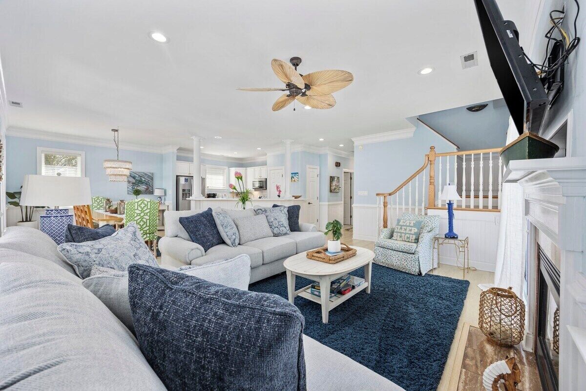 A spacious living room with a ceiling fan, a fireplace, and a staircase.