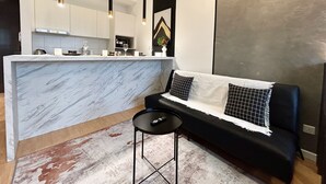 A modern kitchen with a marble island, black and white sofa, and pendant lighting. - Chambers Residence by Manhattan Group  (Kuala Lumpur)