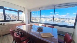 Ein Essbereich mit einem großen Tisch und roten Stühlen, großen Fenstern mit Blick auf eine Marina und einer Holzkabine mit Dekorationen.