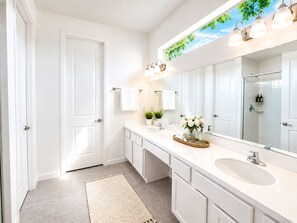 A modern bathroom with a large mirror, white cabinetry, and a shower area.
