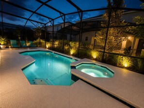 A swimming pool with a hot tub, surrounded by lounge chairs and plants, under a covered area.
