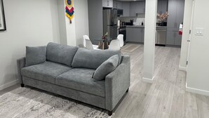 A modern living room with a grey sofa, a dining area with white chairs, and a kitchen with grey cabinets. - Entire guest suite in Calgary (Calgary)
