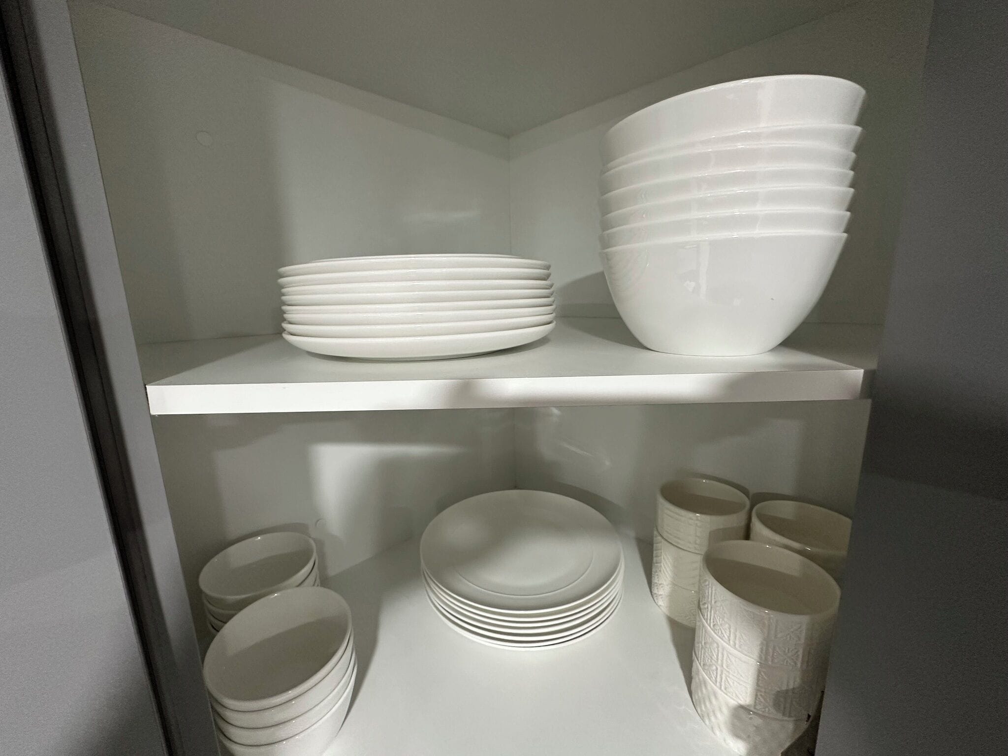 Un espacio de almacenamiento con estantes que contienen cuencos, platos y tazas blancos.