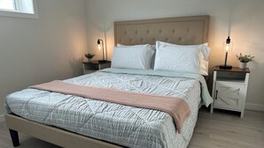 A neatly made bed with a patterned duvet, two bedside tables with lamps, and a window to the left. - Entire guest suite in Calgary (Calgary)