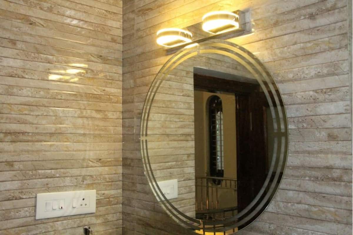 A bathroom with a marble wall, a round mirror with a glass frame, and two wall-mounted lights.
