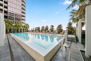 Relax by the rectangular pool surrounded by palm trees and lounge chairs.