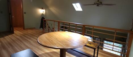 Una habitación amplia con una mesa redonda de madera y un banco, un ventilador de techo y un tragaluz.