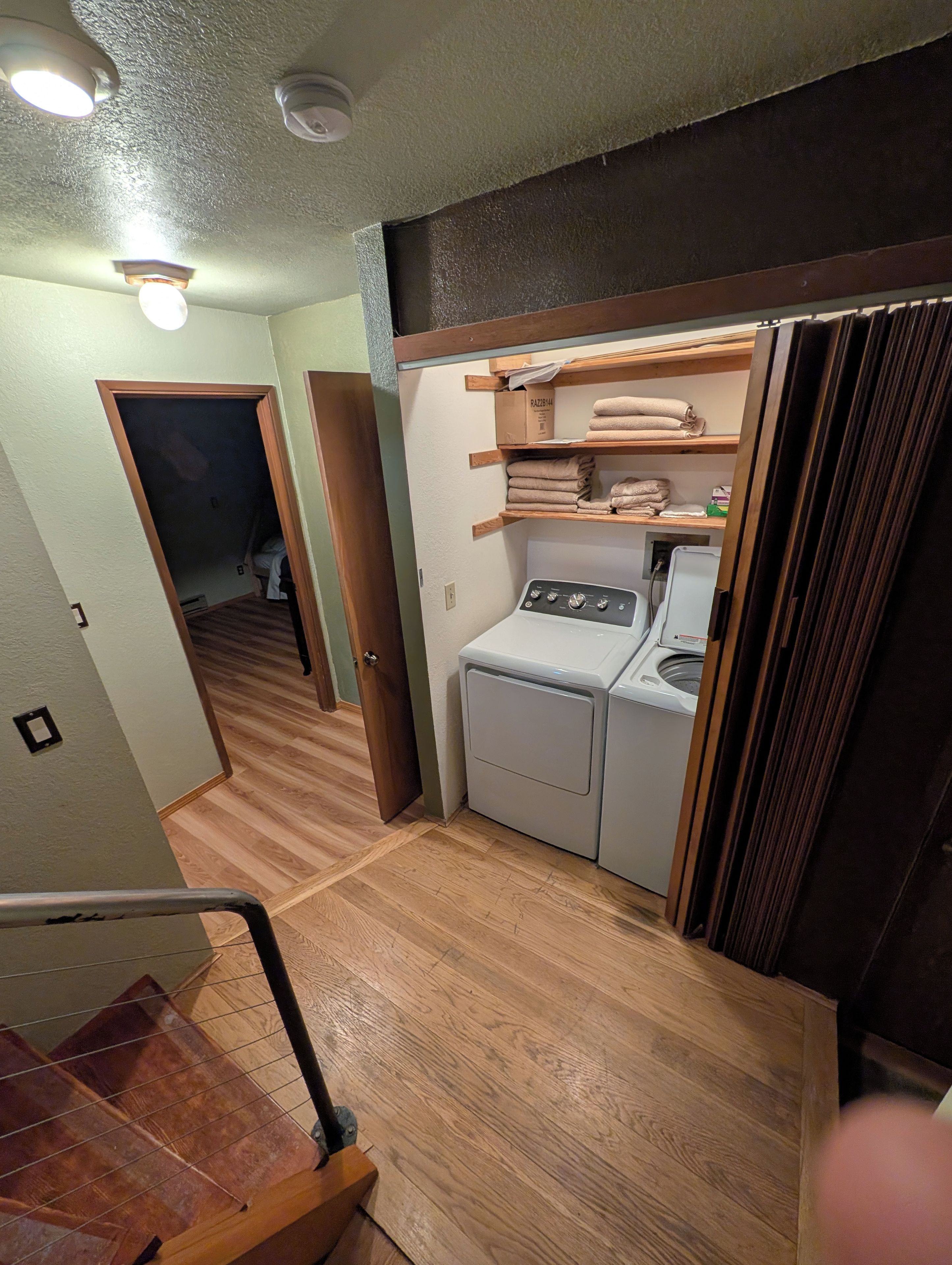 A laundry area with a washing machine, a wooden shelf with folded towels, and a door leading to another room.