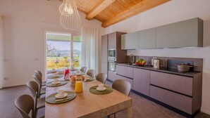 A modern kitchen with a dining area, featuring a wooden ceiling, a large window with a view, and contemporary appliances.
