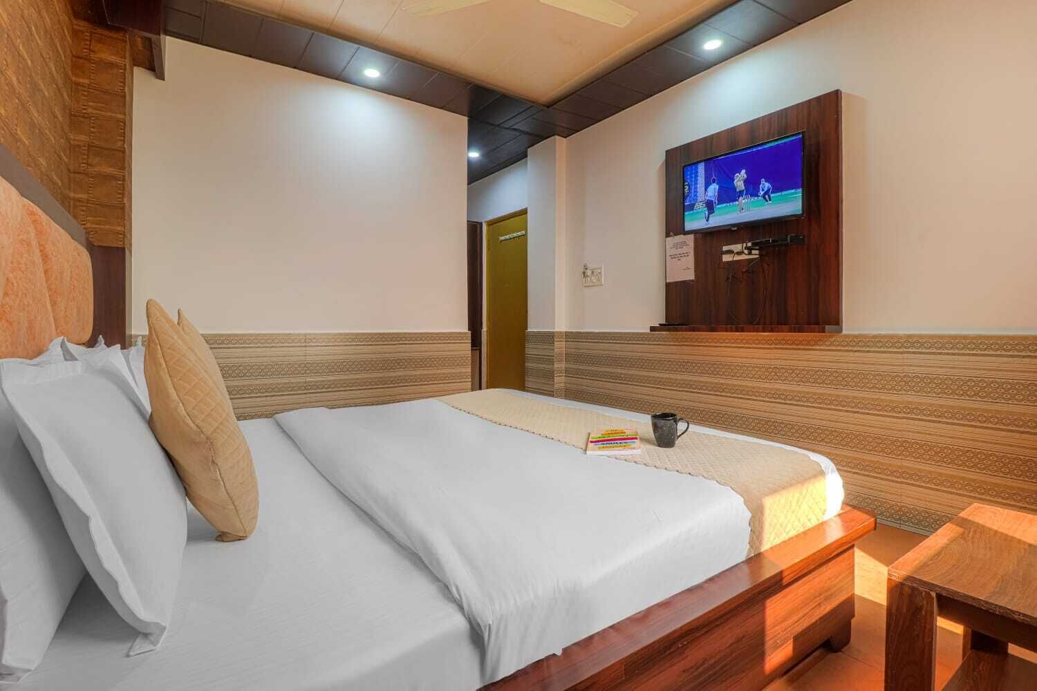 A hotel room with a bed, a TV mounted on the wall, and a wooden bench.
