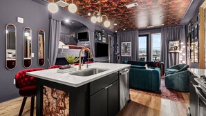Une cuisine moderne avec un îlot central, un coin repas doté d’une chaise rembourrée de couleur rouge, et un salon avec un canapé de couleur turquoise.