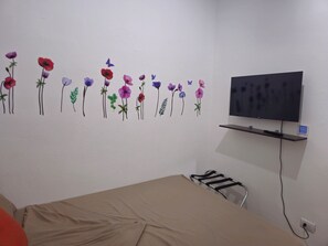 A room with a bed, a TV mounted on the wall, and a wall decoration of flowers.