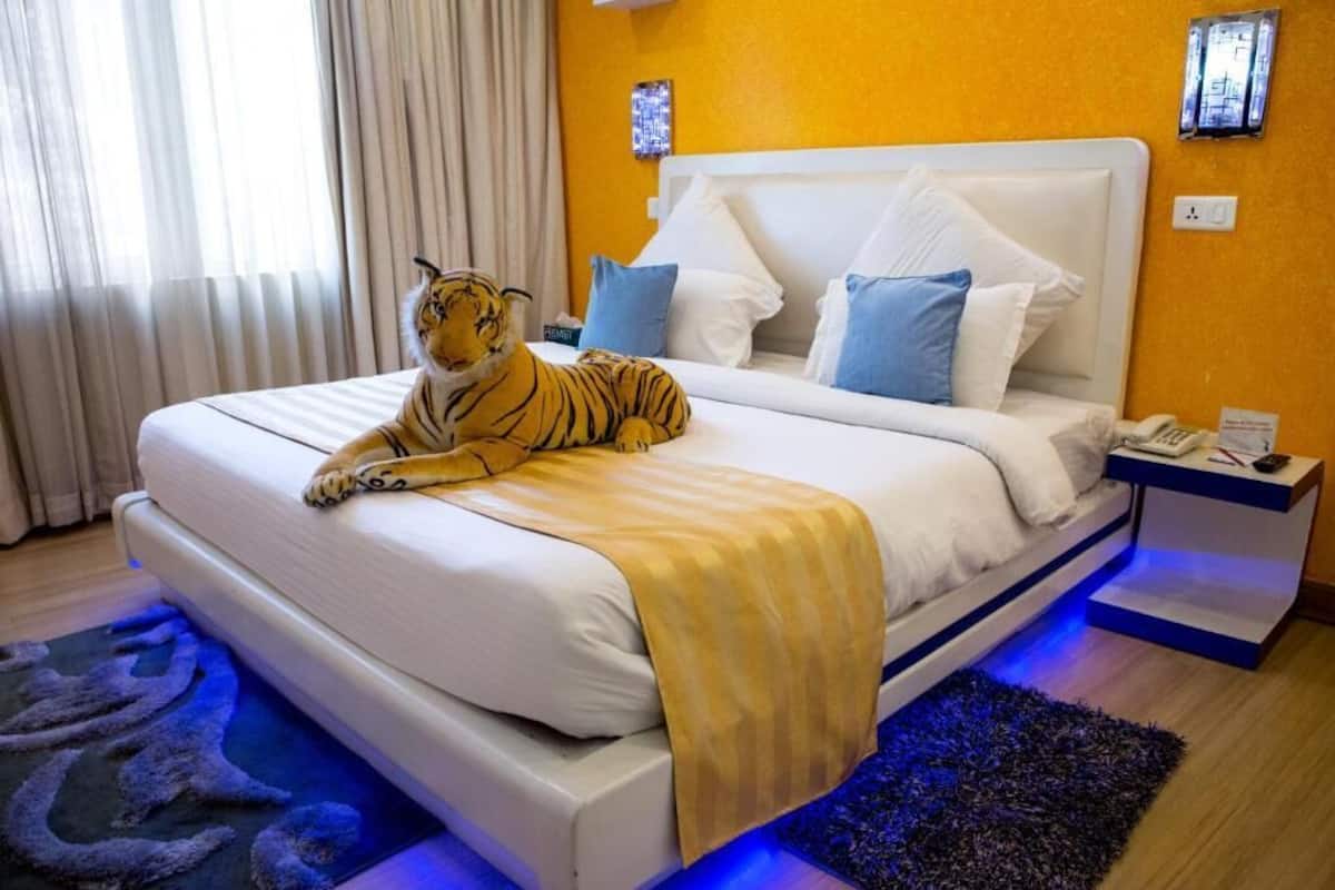 Una cama con un peluche de tigre, ropa de cama blanca, almohadas azules y una alfombra iluminada con luz azul.
