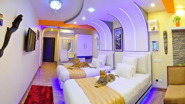 Ein modernes Hotelzimmer mit gewölbter Decke, einem roten Teppich, zwei Betten mit Leopardenmuster-Bettwäsche und einer kleinen Sitzecke.