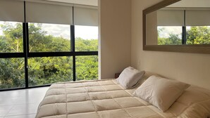 Ein modernes Schlafzimmer mit einem großen Bett, einem Fenster mit Blick auf Grünflächen und einem Spiegel an der Wand.