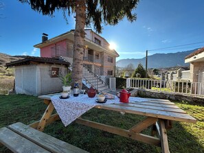 A wooden picnic table set outdoors with a tablecloth, a bottle, a teapot, and a cup.