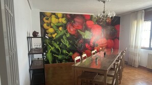 Comedor con una larga mesa, sillas, una araña y un mural en la pared con motivos vegetales.