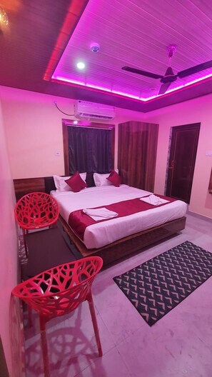 A bedroom with a bed, a ceiling fan, a red chair, and a patterned rug. - Hotel Swarna Lata (Puri)