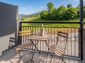 A balcony with a table and chairs, a wine bottle, and a view of a green landscape with trees and mountains.