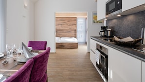 Una cocina moderna con techo de madera, zona de comedor con sillas moradas y una cama con paneles de madera al fondo.