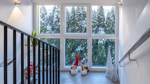 Una escalera con barandilla, una ventana que ofrece vistas a árboles cubiertos de nieve y un pequeño árbol de Navidad.