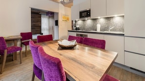 Un área de comedor moderna con una mesa de madera y sillas moradas, una cocina con microondas y pileta, y una escalera que conduce a un nivel superior.
