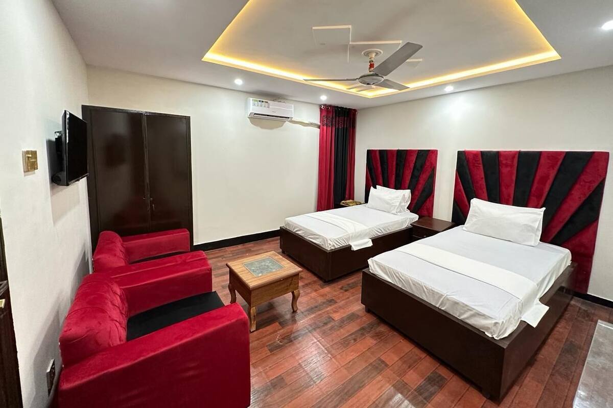 A hotel room with two beds, a TV, a ceiling fan, and a red sofa.