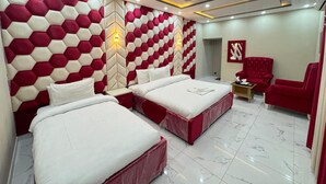 A modern hotel room with a geometric patterned headboard, two beds, a red armchair, and a ceiling fan. - Serene Inn F10 (Islamabad)