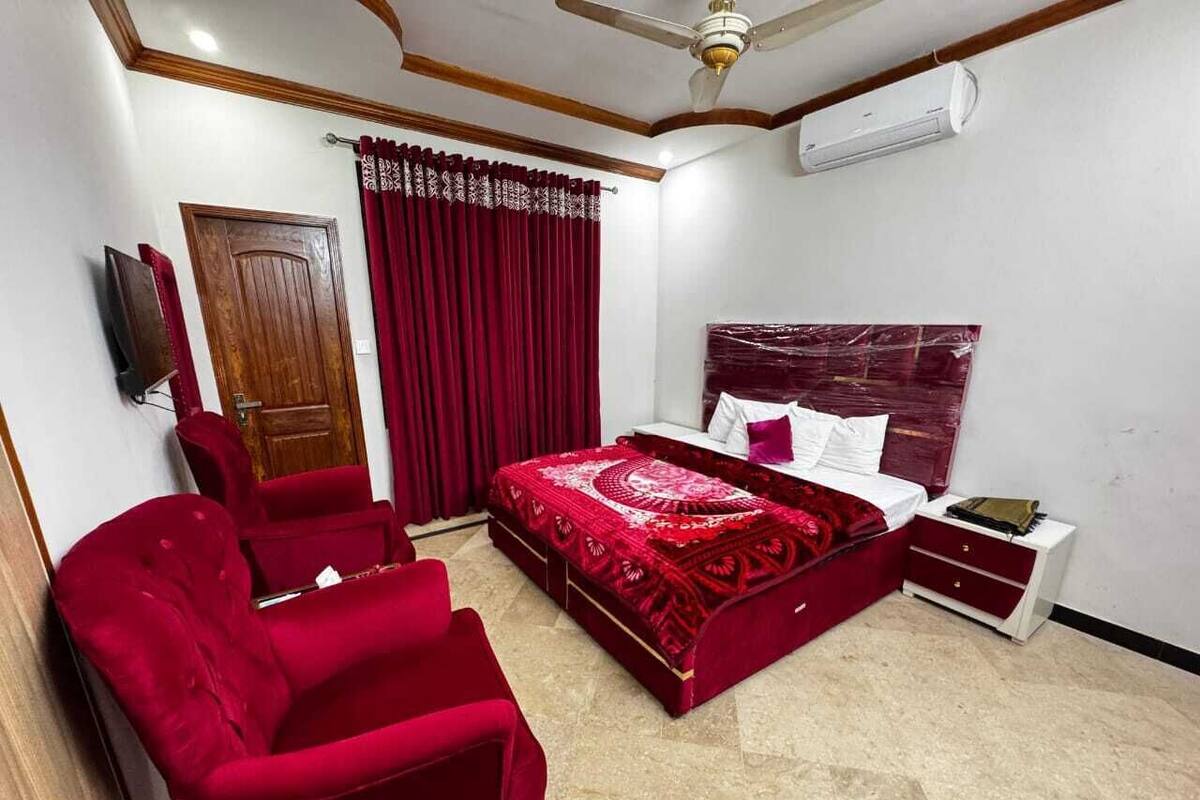 A bedroom with a bed, a red armchair, a nightstand, and a ceiling fan.