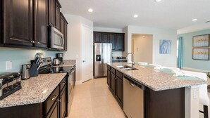 A modern kitchen with dark cabinetry, granite countertops, stainless steel appliances, and a central island with a sink.