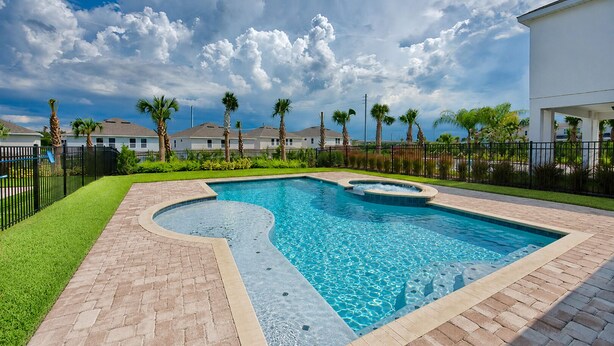 A rectangular swimming pool with a curved edge, surrounded by a brick patio and a fence.