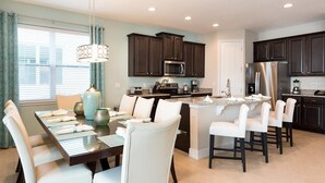 A modern kitchen with dark cabinets, a central island, and a dining area with white chairs.