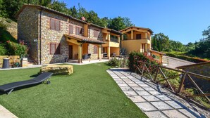Il s’agit d’un bâtiment en pierre à deux étages, doté d’une façade en pierre et d’une couleur jaune. On y trouve une pelouse bien entretenue, avec un fauteuil de jardin et un chemin en pierre menant au bâtiment.