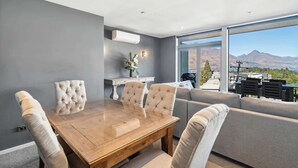 Un espace repas moderne avec une table en bois et des chaises rembourrées, un canapé gris et une grande fenêtre donnant sur une vue imprenable sur les montagnes.