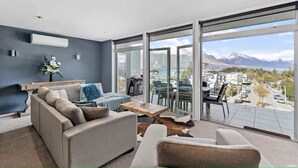 Un salon moderne avec un canapé, une table basse et une vue sur les montagnes, visible à travers de grandes portes vitrées.