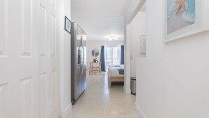 Ein moderner Hotelkorridor mit Küchenbereich, Esstisch und einem Schlafzimmer mit Bett und Fenster.