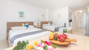 Ein Hotelzimmer mit zwei Betten, einem Holzkopfteil, einem Nachttisch mit Lampe, einer kleinen Topfpflanze und einer Obst- und Gemüsetafel.