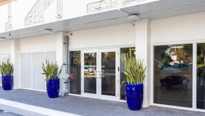 Ein Gebäude mit heller Fassade, großen Glasüren und blauen Pflanzgefäßen mit Grünpflanzen.