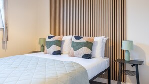 Ein ordentlich bezogenes Bett mit einer gesteppten Decke, zwei Kissen mit geometrischem Muster und zwei Nachttische mit Lampen.