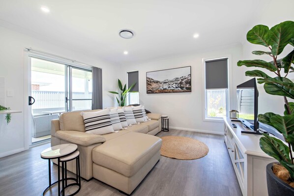 A modern living room with a beige sectional sofa, a small round table, and a large potted plant.
