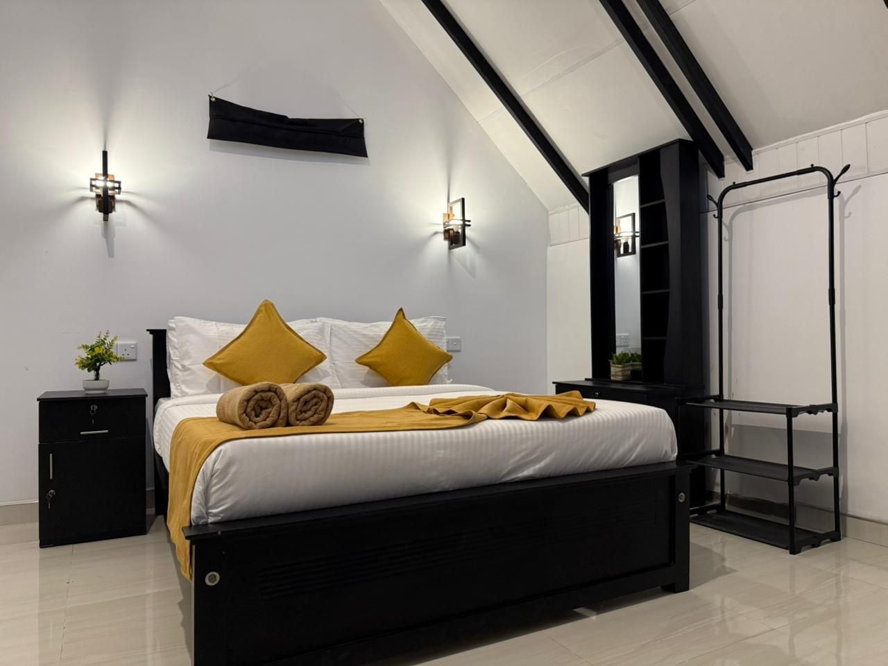 A modern bedroom with a black bed, white bedding, and two wall-mounted lights.