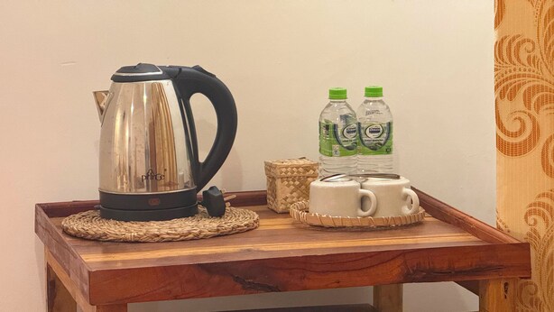 A wooden tray with a kettle, two bottles of water, and two mugs on a woven mat. - Tera Ella Boutique Hotel by SANS (Ella)