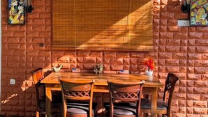 A brick wall with a wooden table and chairs, a window with a blind, and decorative wall art. - Tera Ella Boutique Hotel by SANS (Ella)