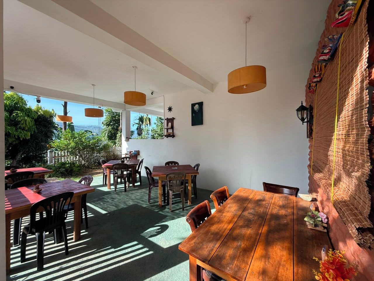 Un comedor con mesas y sillas de madera, una pared de ladrillo con detalles decorativos y lámparas colgantes.