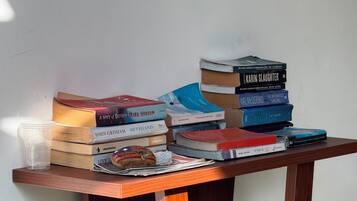 A stack of books on a wooden table with a clear plastic cup and a pastry.